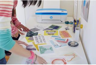 Two girls look through photographs and artwork printed on a HP DeskJet 3720 All-in-One.