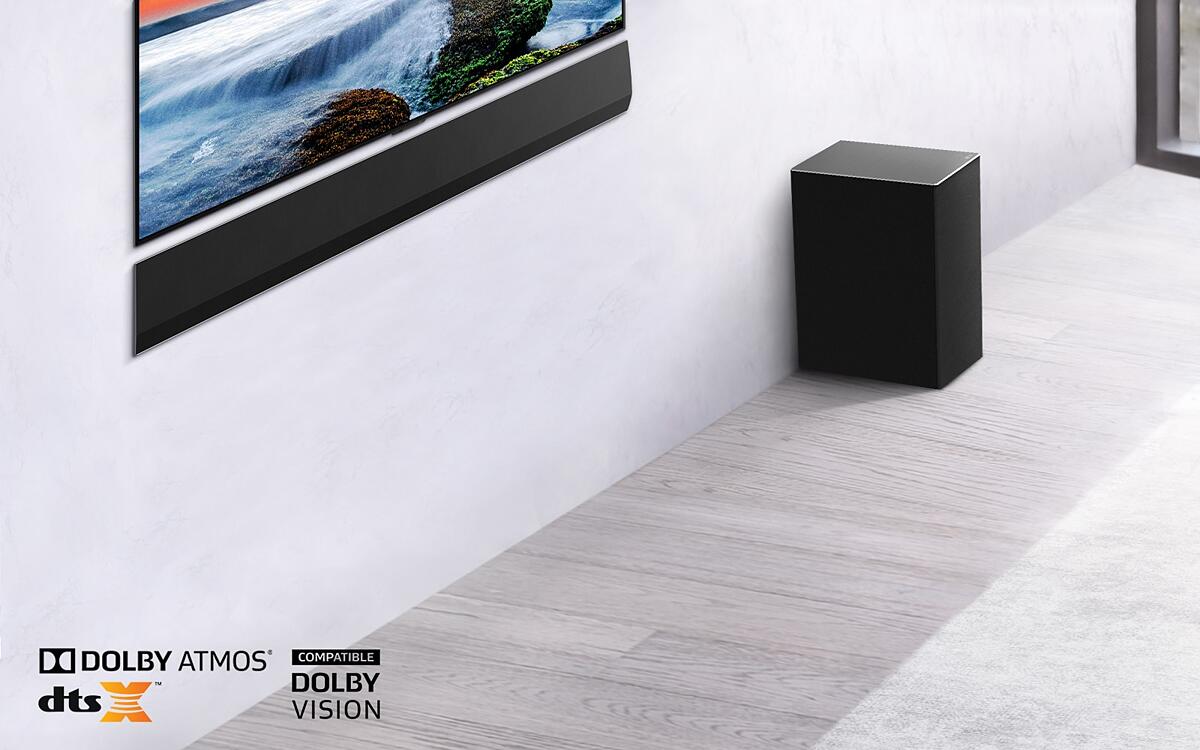 The TV and LG Soundbar are wall-mounted with a sub-woofer below and to the right. The TV shows a sunset at sea.