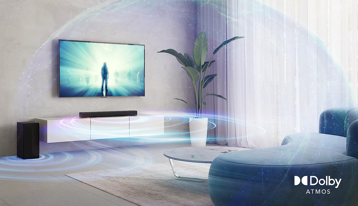 In the living room, LG TV is on the wall. A moive is playing on TV screen. LG Soundbar is right below TV on a beige shelf with a rear speaker is placed on left. Dolby Atmos Virtual logo shown on right