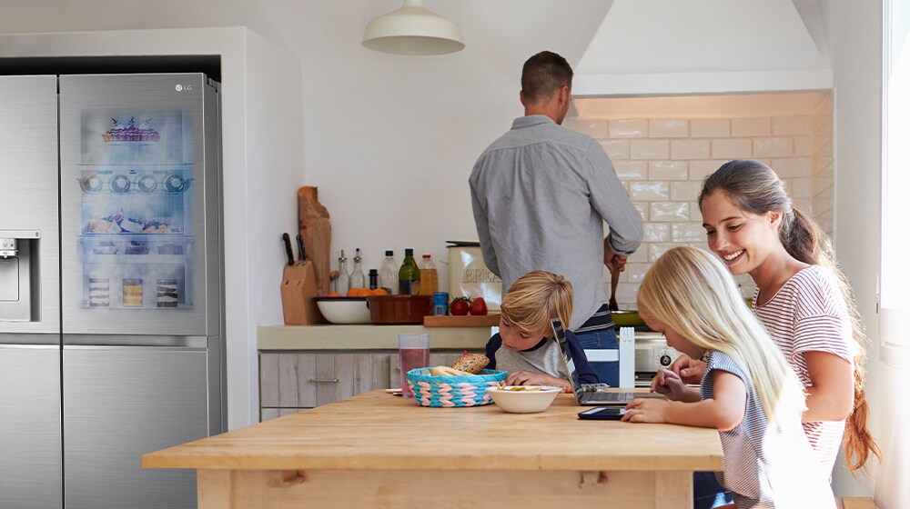 Family in modern kitchen; children using tablets at table, man cooking near LG refrigerator.