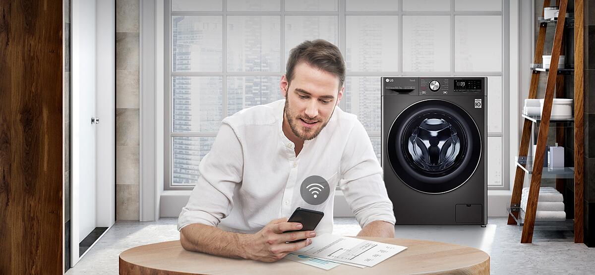 A man is monitoring the condition of the washing machine through a mobile phone app.