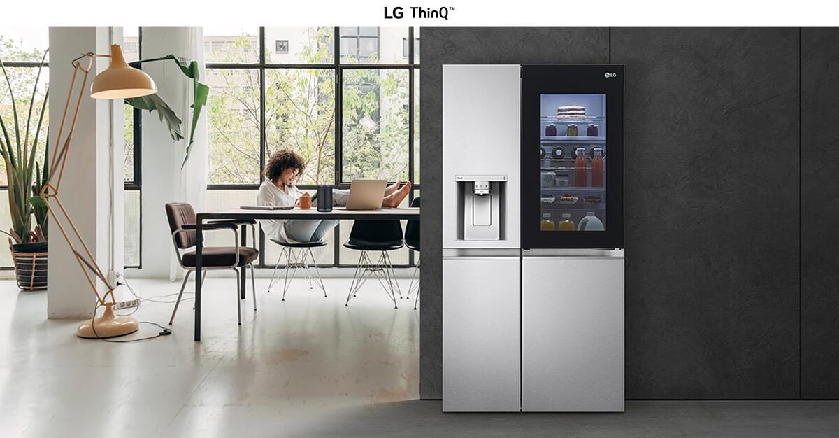 Sleek silver LG ThinQ fridge on right, modern kitchen with large windows on left, inviting and functional.