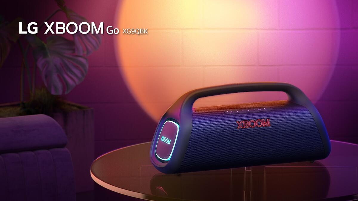 LG XBOOM Go XG9 is placed on the metal table with orange lighting is on. Behind the table, stage lighting is spotlighting the wall.